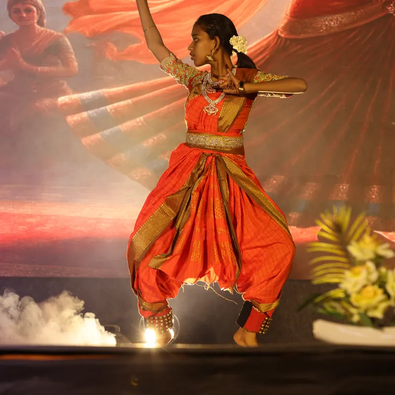 Classical dancer mid-leap in an orange sari against a dramatic stage backdrop