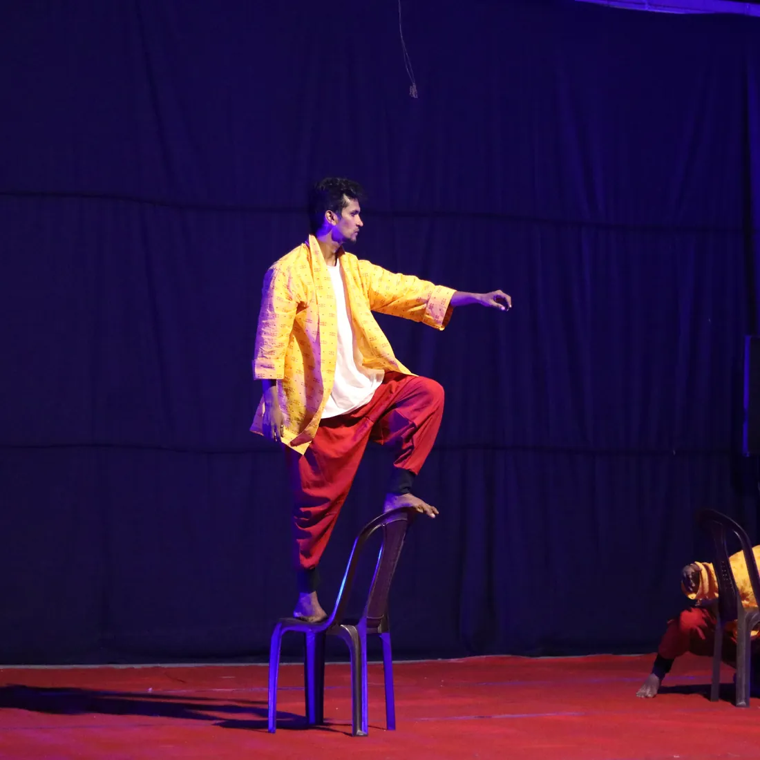 Solo dancer in a yellow jacket balanced on a stool mid-performance
